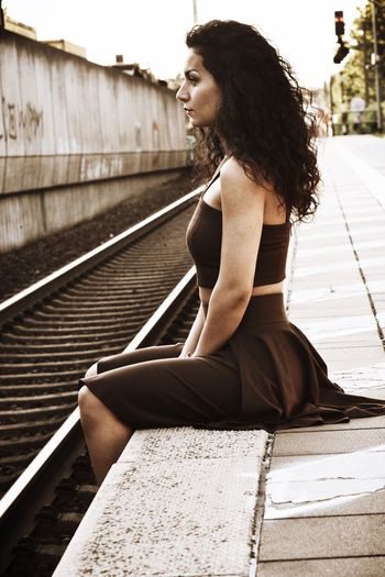 Side view of young woman sitting on railroad track