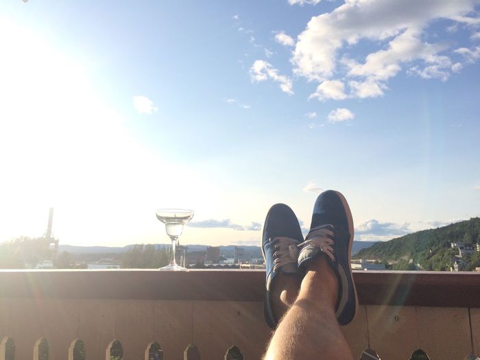Low section of man feet on railing with martini glass against sky