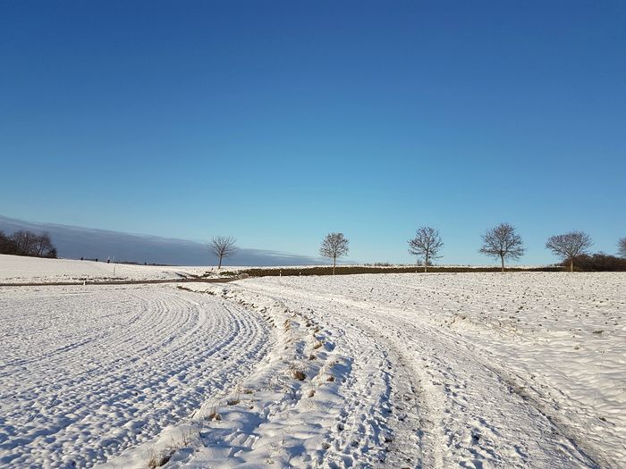 Tire tracks on snow covered land against clear blue sky