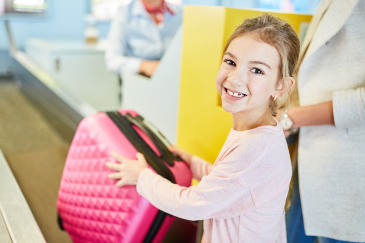 Portrait of smiling girl holding suitcase at airport