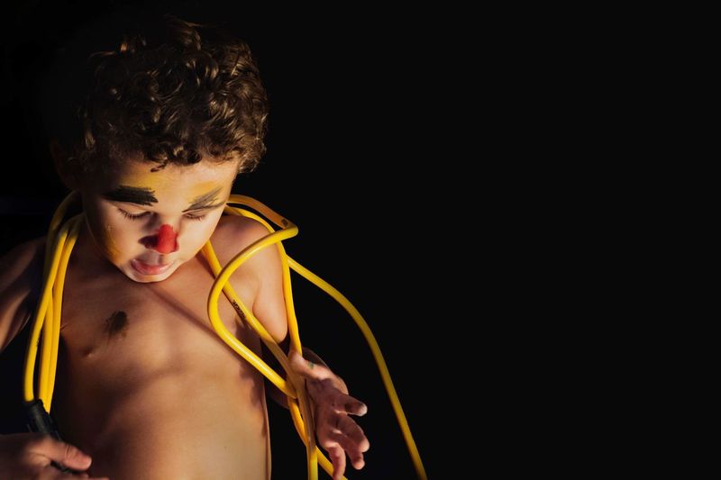 Shirtless boy with face paint and yellow cables standing against black background