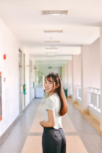 Portrait of young woman standing at corridor in building