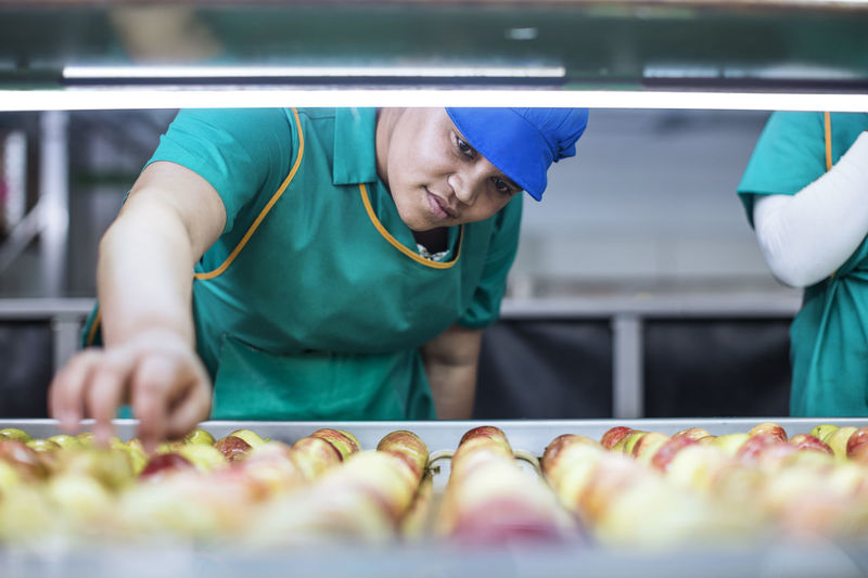 Female worker checking apples on conveyor belt in factory