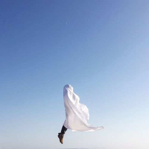 Low section of man covered with cloth jumping against clear blue sky