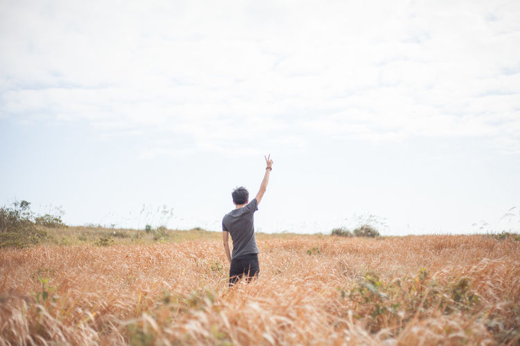 Rear view of man gesturing peace sign on agricultural field against sky