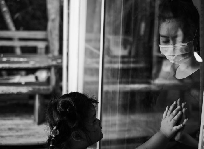 Mother wear face mask meeting daughter and touching hand through the window
