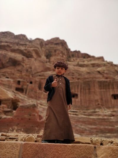 Boy standing on mountain in desert against clear sky