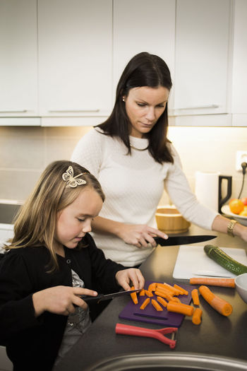 Mother and daughter cutting vegetables in kitchen