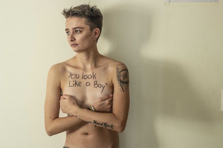 Shirtless young woman with text on body standing against wall