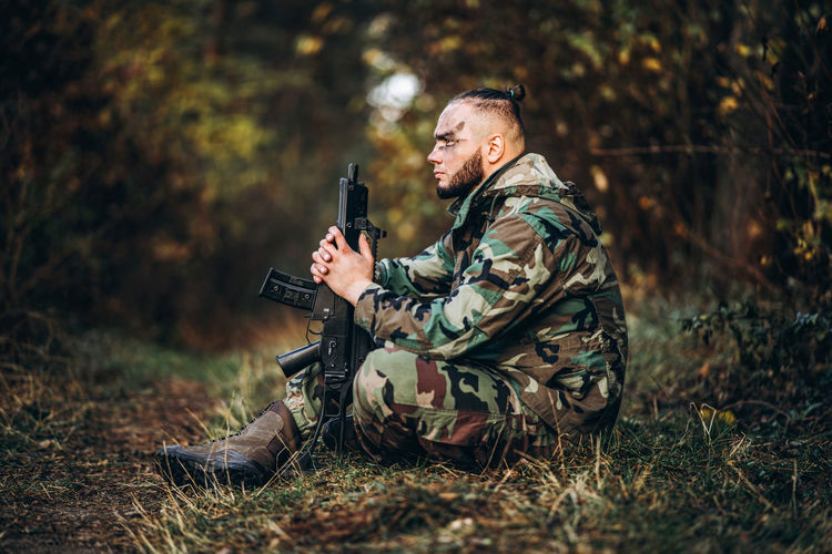 Man holding camera while sitting on land against trees