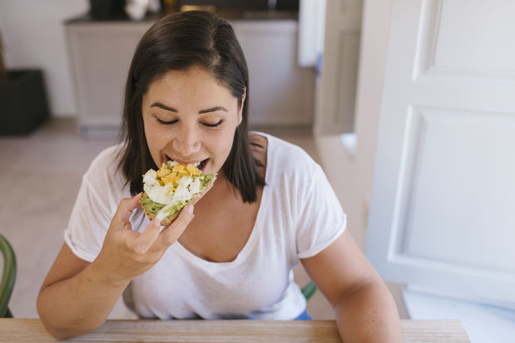 Woman biting a breakfast toast of avocados and eggs