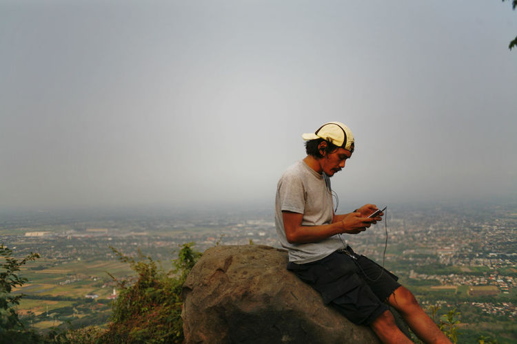 Man sitting on rock in mountain hill against sky