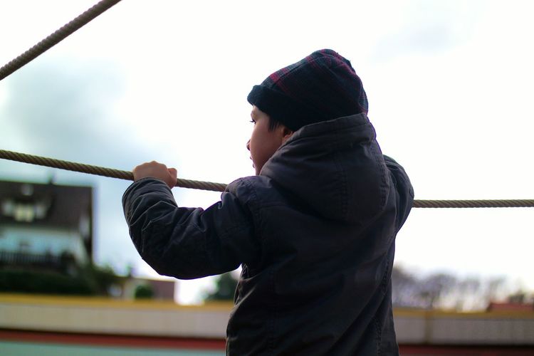 Rear view of boy standing by rope against sky