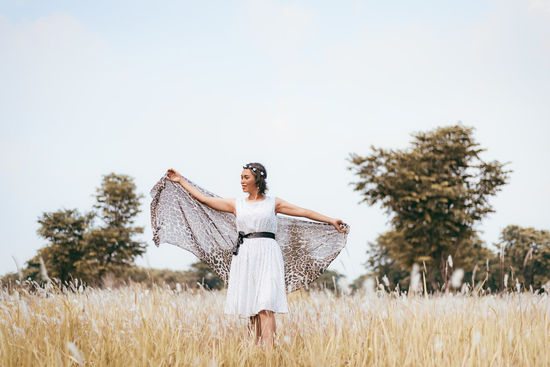 A woman holding a fabric, standing on field against sky