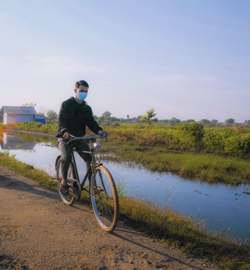 Man riding bicycle on riverbank against sky