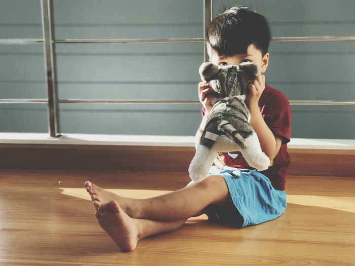 Cute boy sitting with stuffed toy cat at home