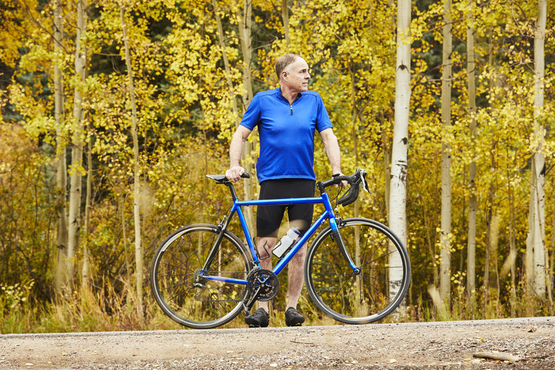 Full length of determined senior man with bicycle standing against trees