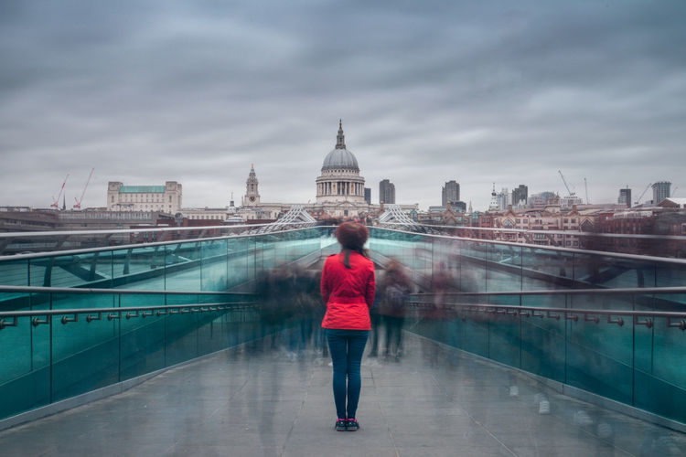 Woman standing on millennium bridge looking at st paul cathedral against sky
