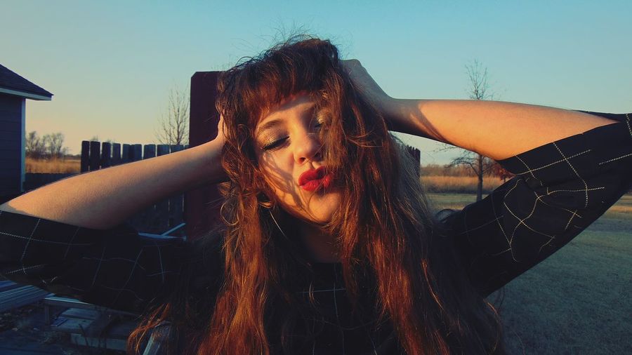 Close-up of young woman puckering against sky during sunset
