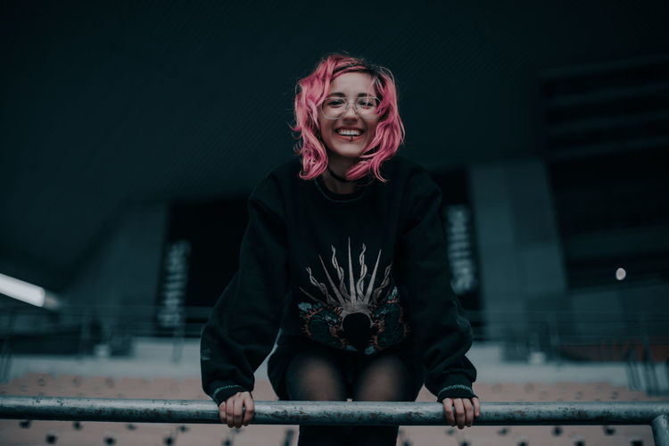 Low angle portrait of smiling young woman with dyed hair standing by railing