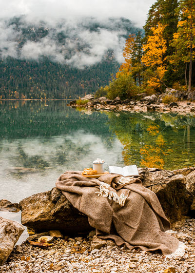 Picnic with plaid, cacao with marshmallow on stones near lake in the bavarian mountains, germany