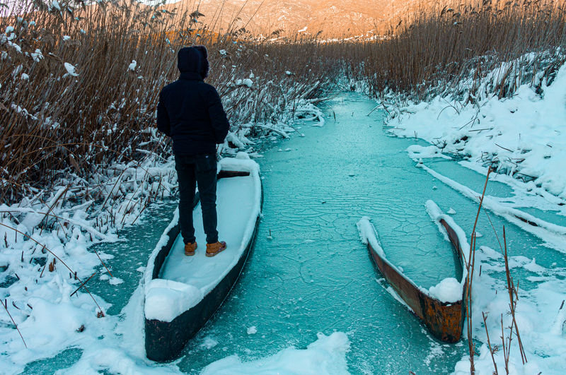 Rear view of man standing in frozen lake during winter