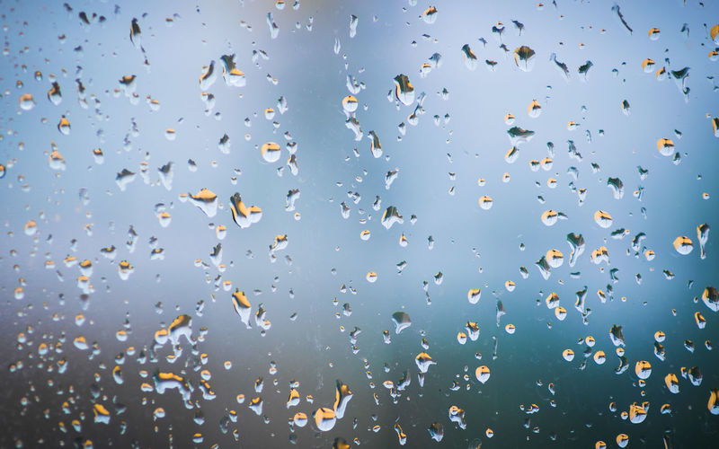 Low angle view of raindrops on glass against sky