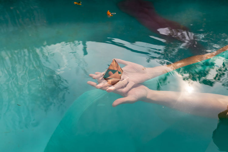 Cropped hand of woman holding pyramid crystal in swimming pool
