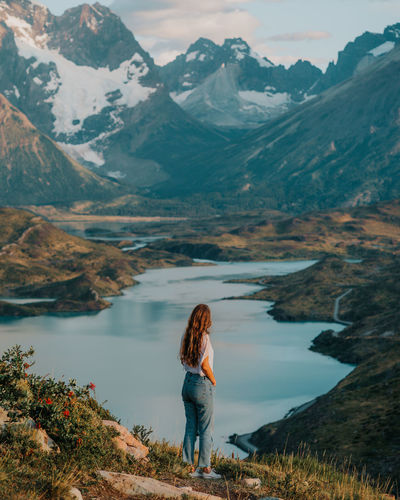 Rear view of woman standing by lake against mountains