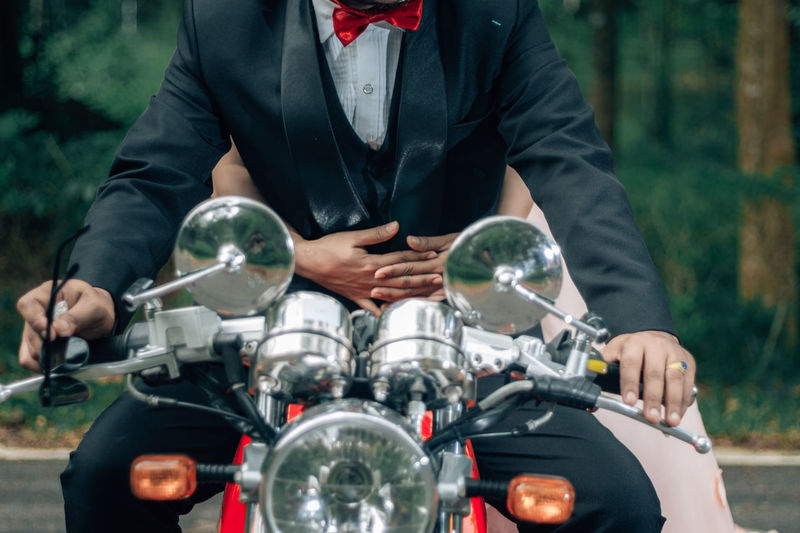 Midsection of bridegroom and bride riding motorcycle on road