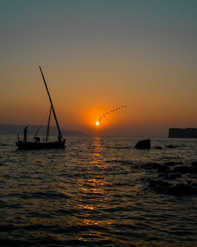 Silhouette sailboat in sea against sky during sunset