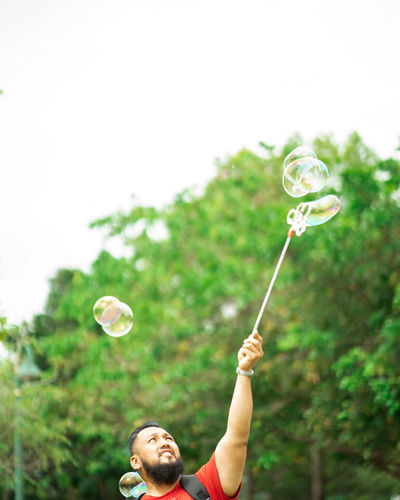 Bearded man playing soap bubbles at the park.