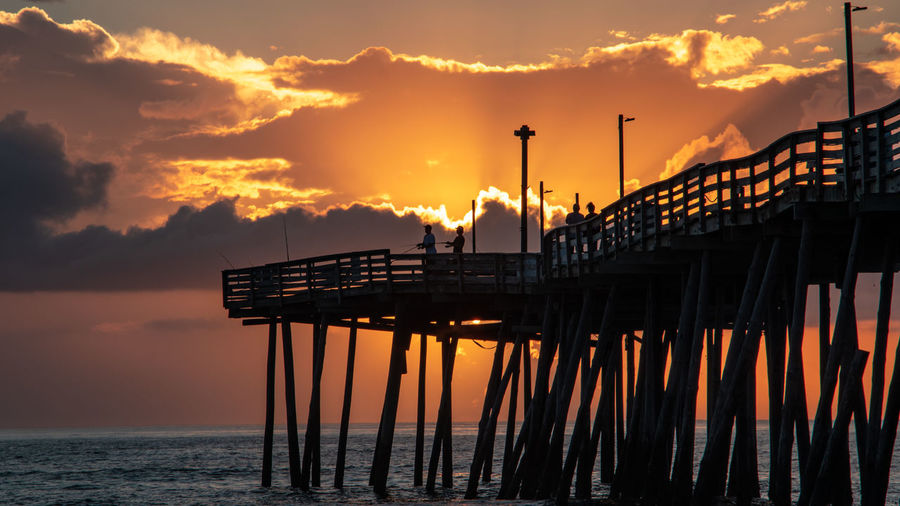 Silhouette pier over sea against sky during sunset