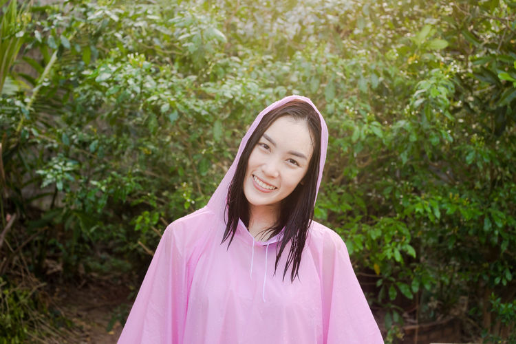 Portrait of young woman in raincoat standing against trees