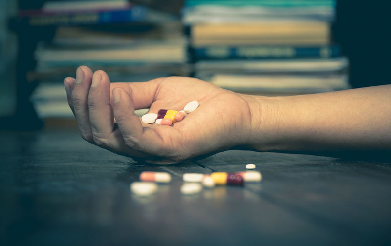 Cropped hand of dead man with medicines on floor at home