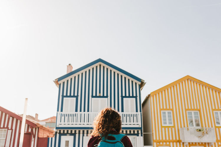 Back view of backpacker woman in front of colorful houses.promenade of costa nova, aveiro, portugal