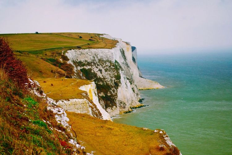 Scenic view of sea by cliff against sky