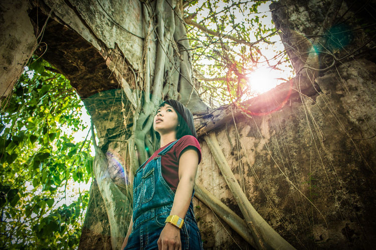 Low angle view of thoughtful young woman looking away while standing in forest