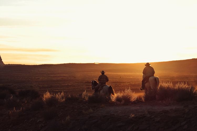 Men riding horse on field against sky during sunset