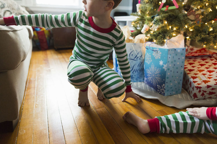 Boy in striped pajamas crouches next to sofa and christmas tree