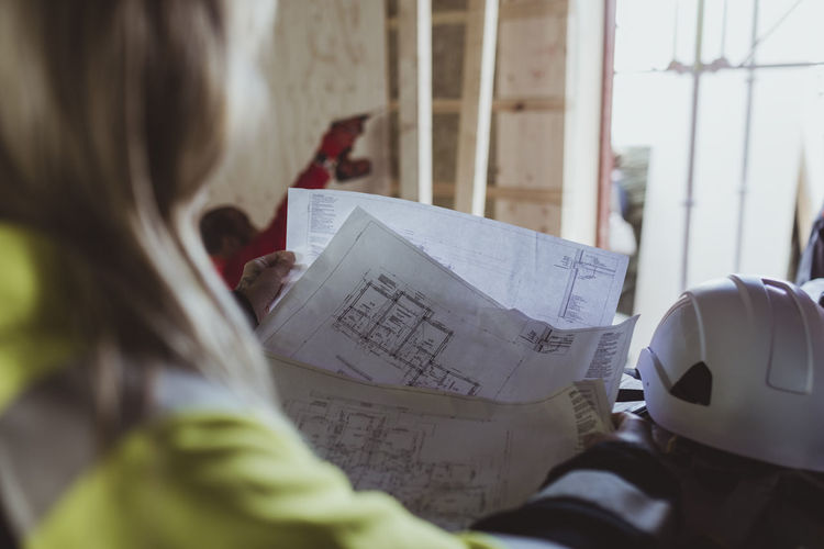 Female builder reading floor plan while analyzing at construction site
