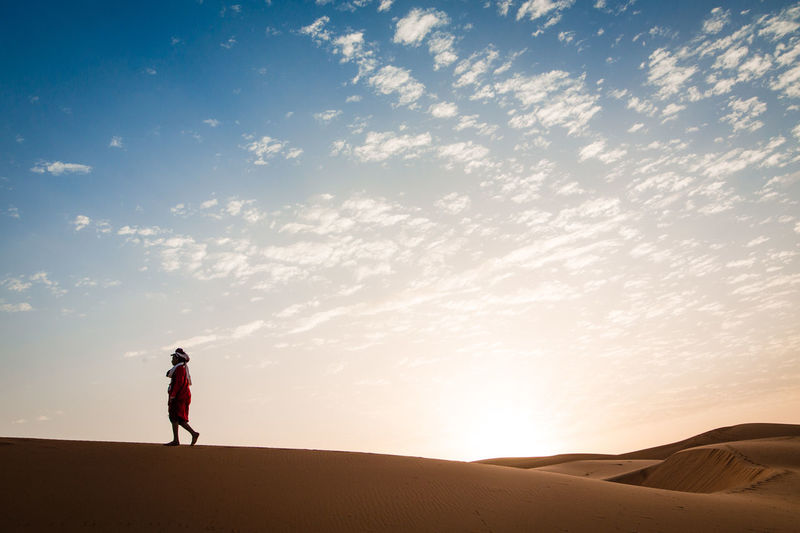 Man standing on sand dune in desert against sky