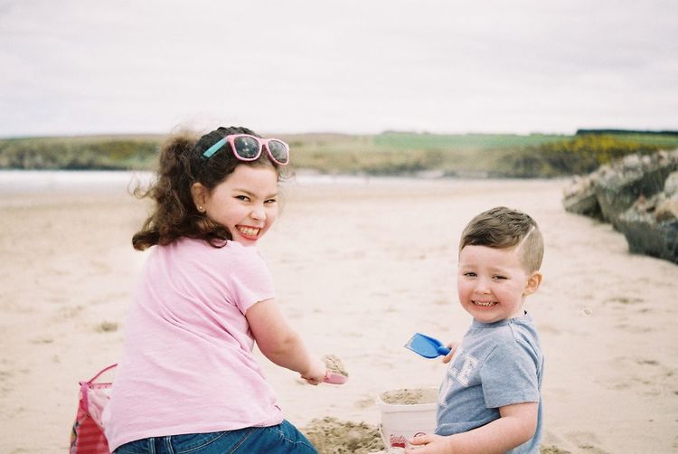 Portrait of happy siblings playing at beach against sky