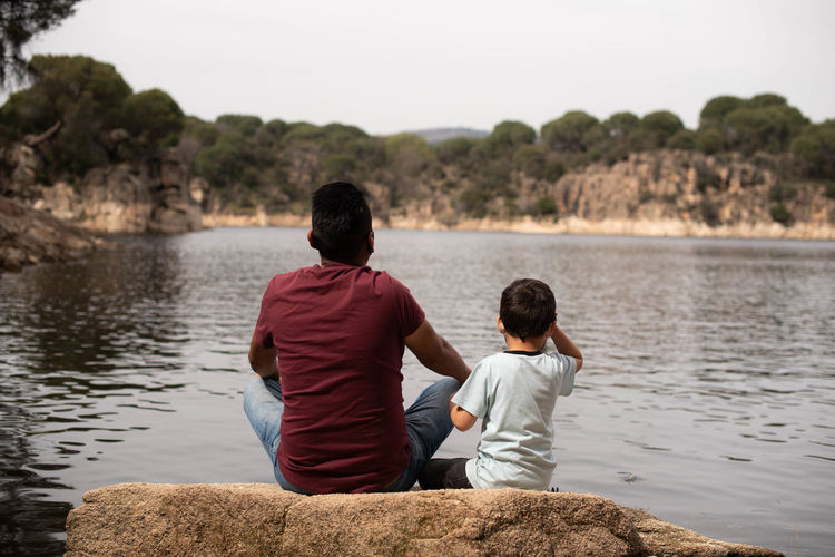 Rear view of father and son sitting on a wide riverside