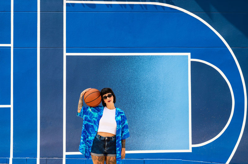 Caucasian girl with sunglasses and tattoos on a blue background with a basketball