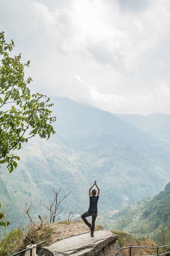 Rear view of woman practicing yoga against mountain