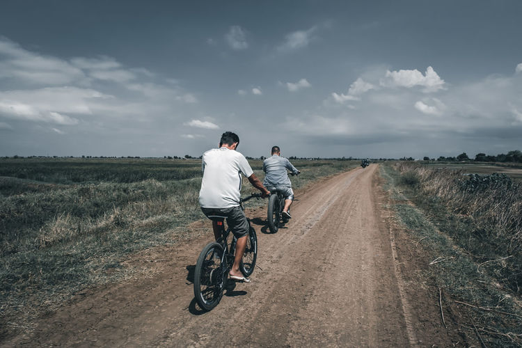 Rear view of man riding bicycle on road against sky