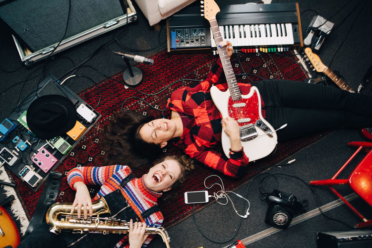 High angle view of happy female musicians playing instruments while lying on carpet