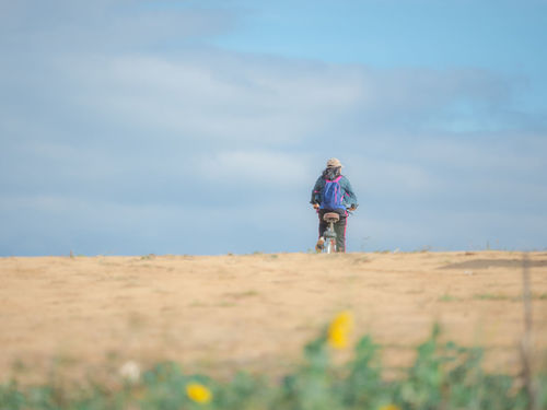 Rear view of woman cycling bicycle on field against sky