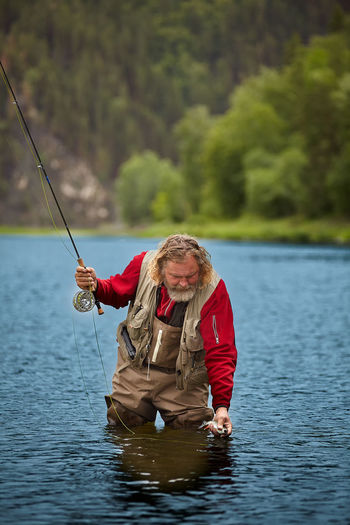 Man fishing in lake against trees